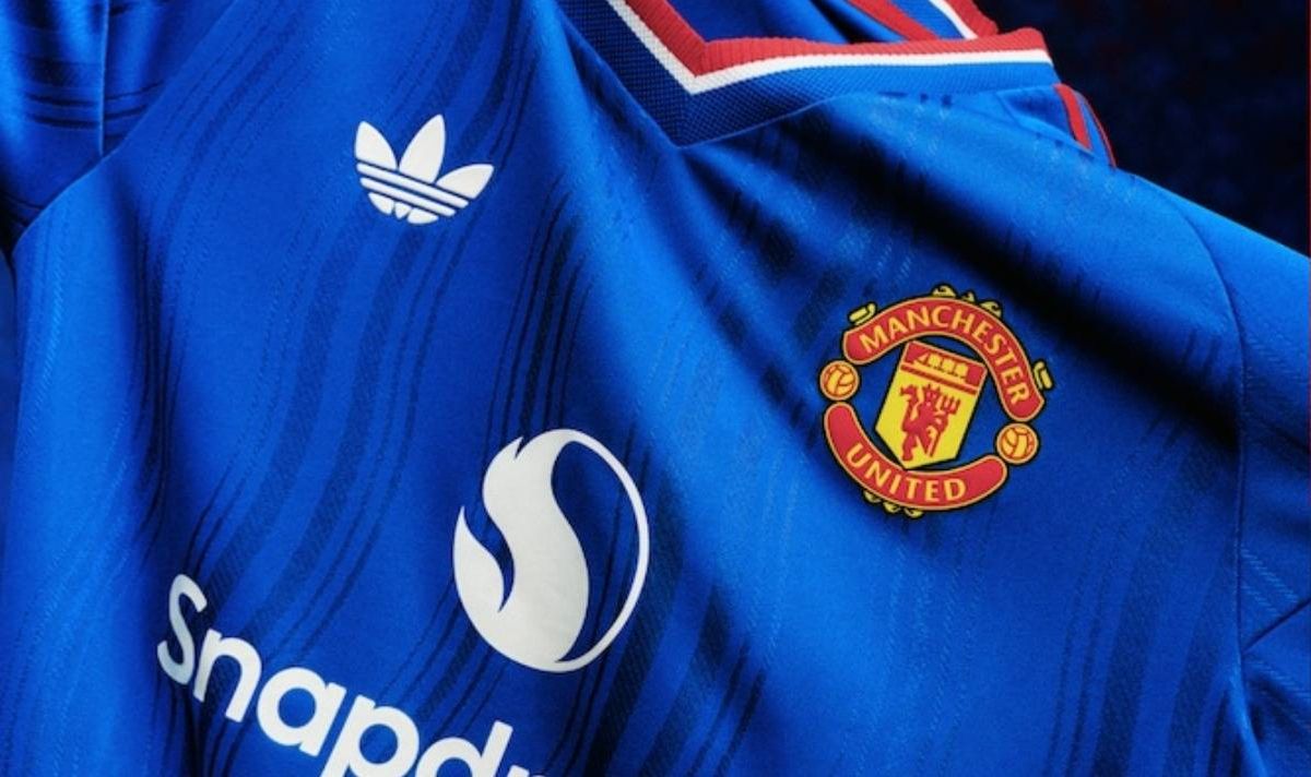 A close-up view of a blue sports jersey featuring a prominent Adidas logo, the Manchester United crest, and the word