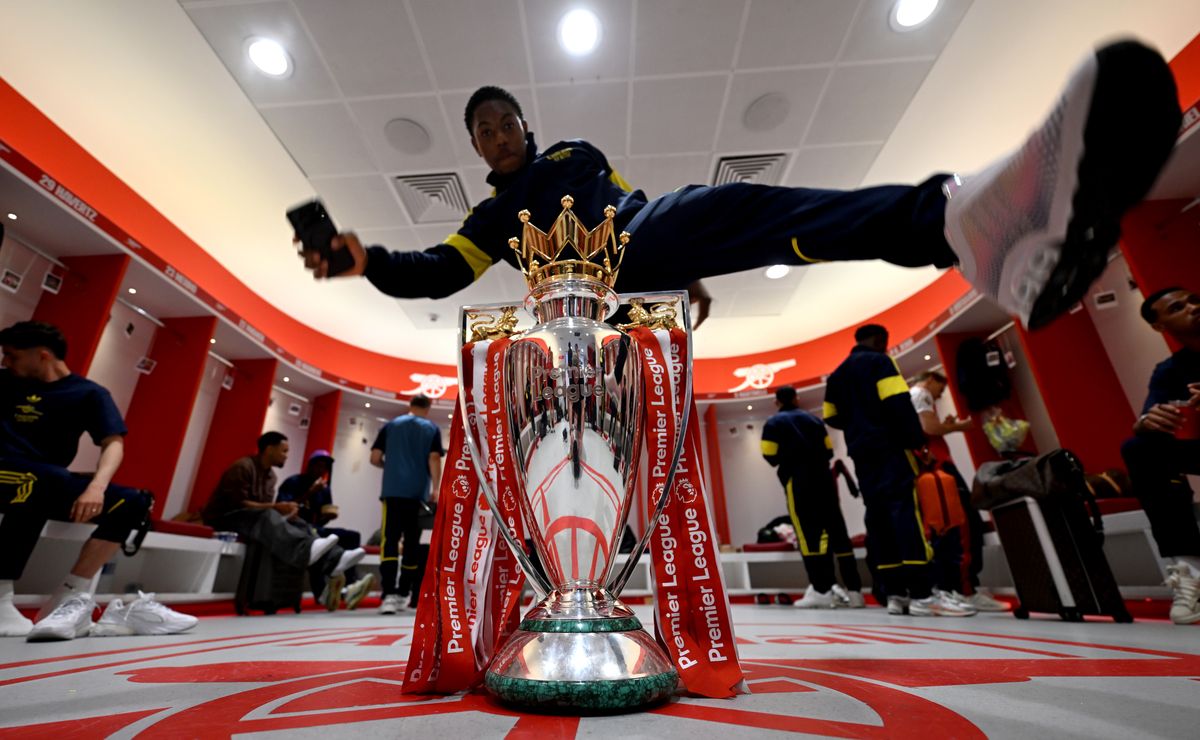 Myles Lewis-Skelly of Arsenal jumps over the Premier League trophy in the Arsenal dressing room