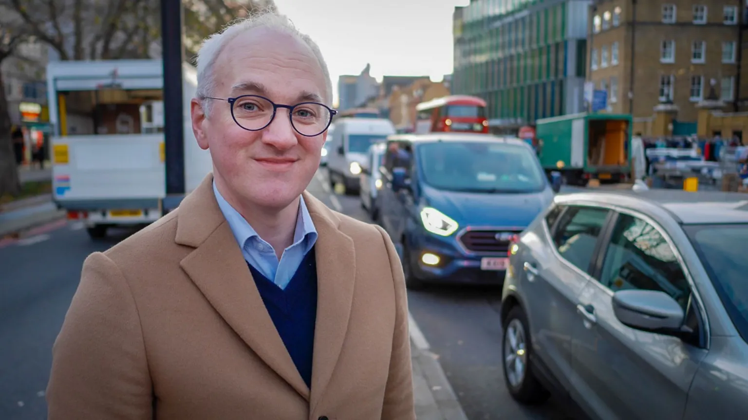 BBC James Gallagher stands on a road busy with traffic.