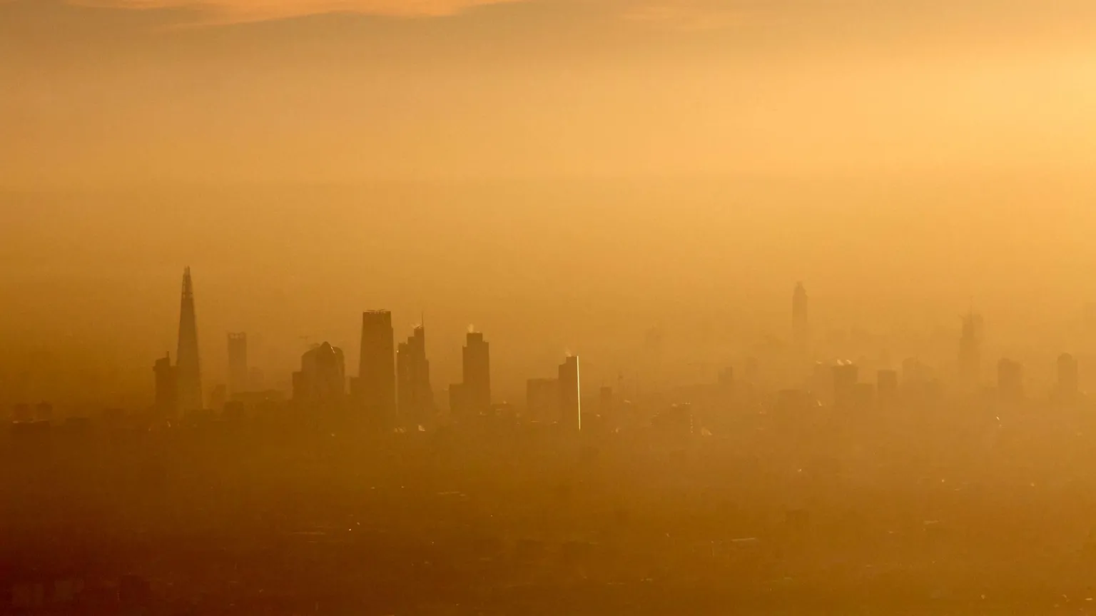  A yellow washed picture that is incredibly hazy, but you can see the outlines of buildings that make up the London skyline