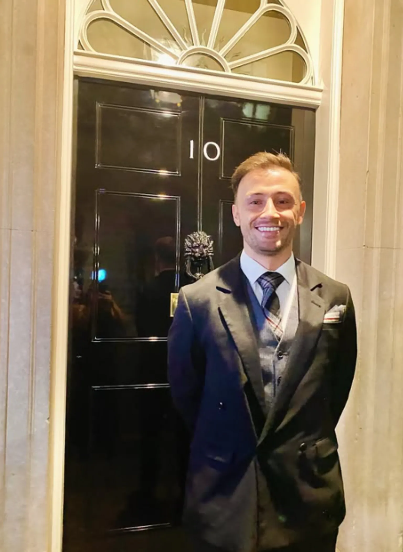 Zander Murray Zander Murray is wearing a dark suit with a tartan tie. He is standing in front of the black door at 10 Downing Street with his hands behind his back while smiling.