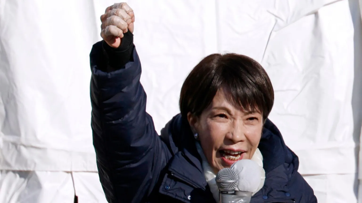 EPA Sanae Takaichi speaks into a microphone with her fist raised. She's wearing a dark blue puffer coat