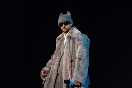man in fur coat, beanie and sunglasses holds microphone