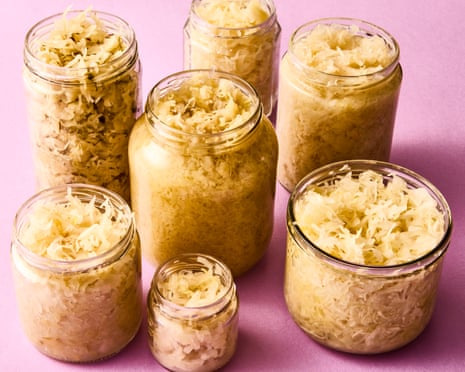 Seven jars of sauerkraut, of varying sizes, photographed against a pink background.