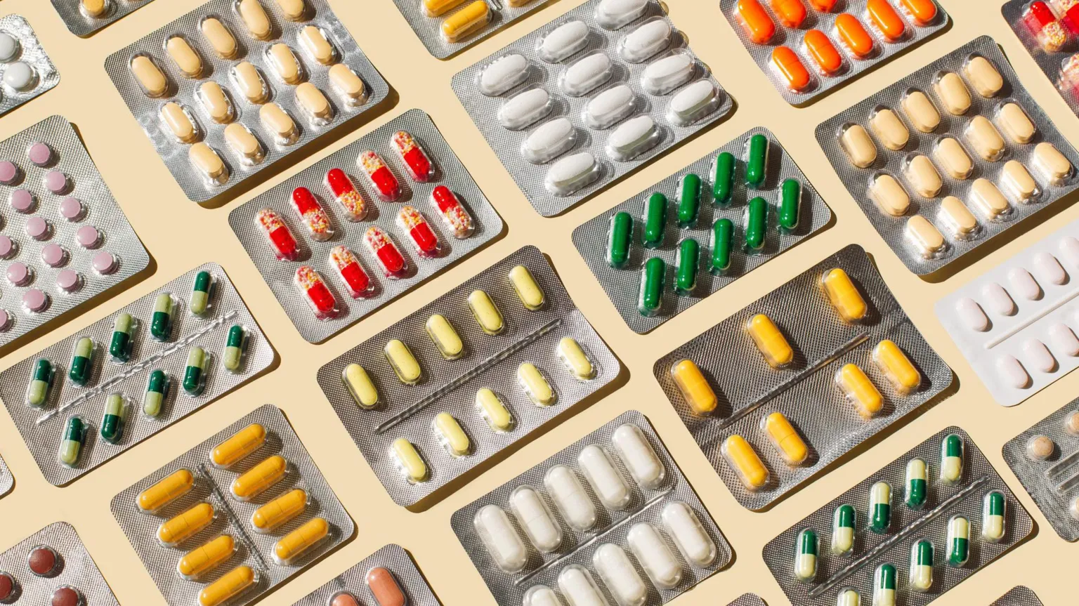  Pattern of blisters with colorful pills and capsules on beige background.