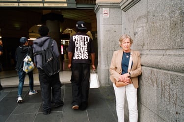 a woman stands on the street looking at camera next to some men who have their backs to the camera, one with the words “Pretty Girls Love Jesus” on his t shirt