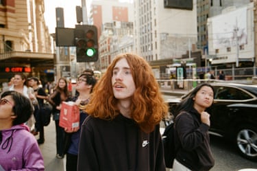 a man with long red hair and a moustache looks off camera on an intersection