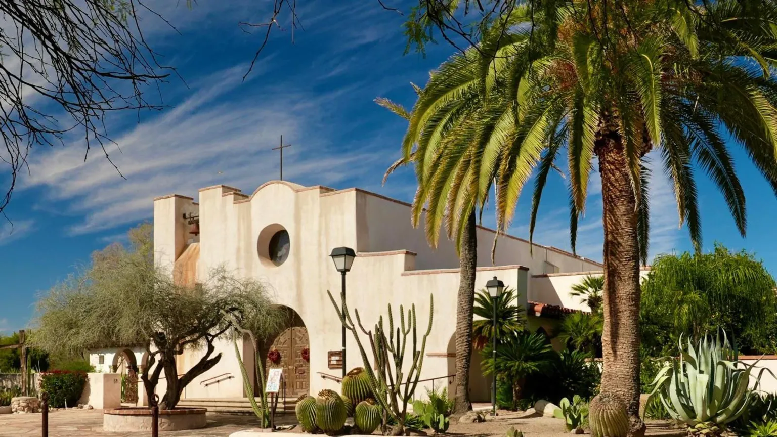 St Philip’s in the Hills Episcopal church - where Nancy Guthrie worshiped and where they held a vigil for her. The church is a white building with a terracotta paving in the front with cacti surrounding the building 