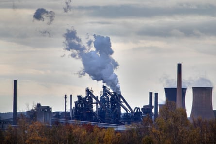 View of Scunthorpe site from a distance with chimneys almost silhouetted against a grey, cloudy skyline and trees and greenery in the foreground. 