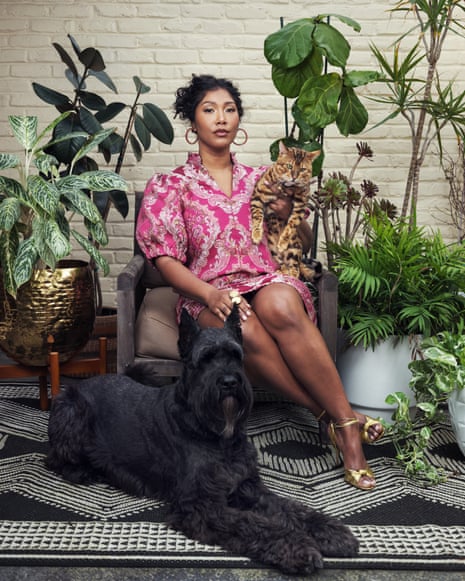 Simone Ledward Boseman, photographed last month. She is seated in a chair wearing a red print dress, holding a tabby cat with a giant schnauzer dog at her feet