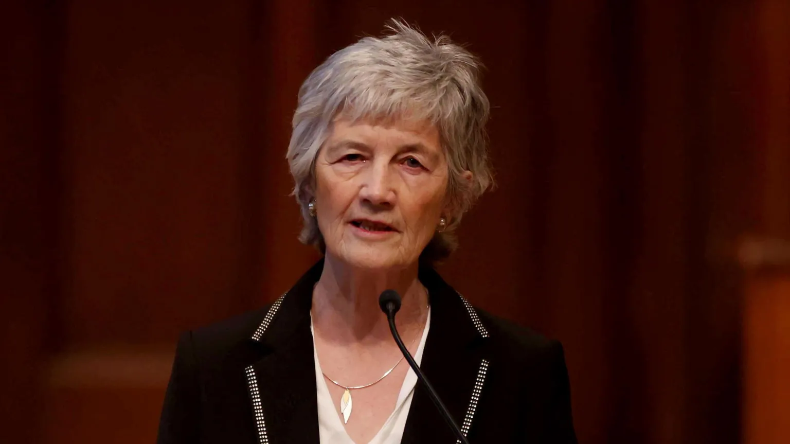  Catherine Connolly speaking into a microphone. She is wearing a white top and a black suit jacket. 