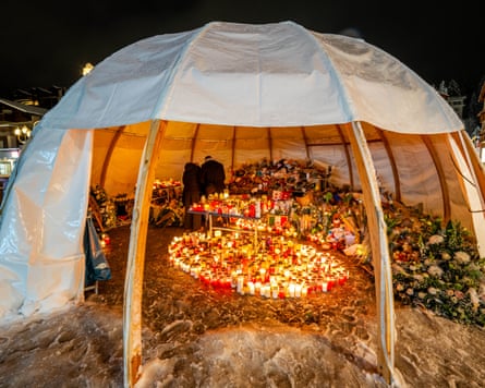 Candles, flowers and messages partially covered by a wood and tarpaulin dome