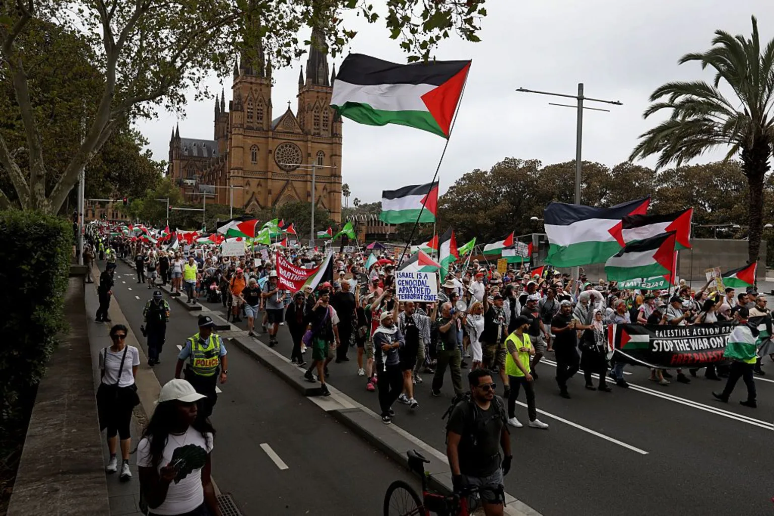 Getty A crowd of people, many waving black, white, red and white flags, march down a city street with a cathedral in the background.