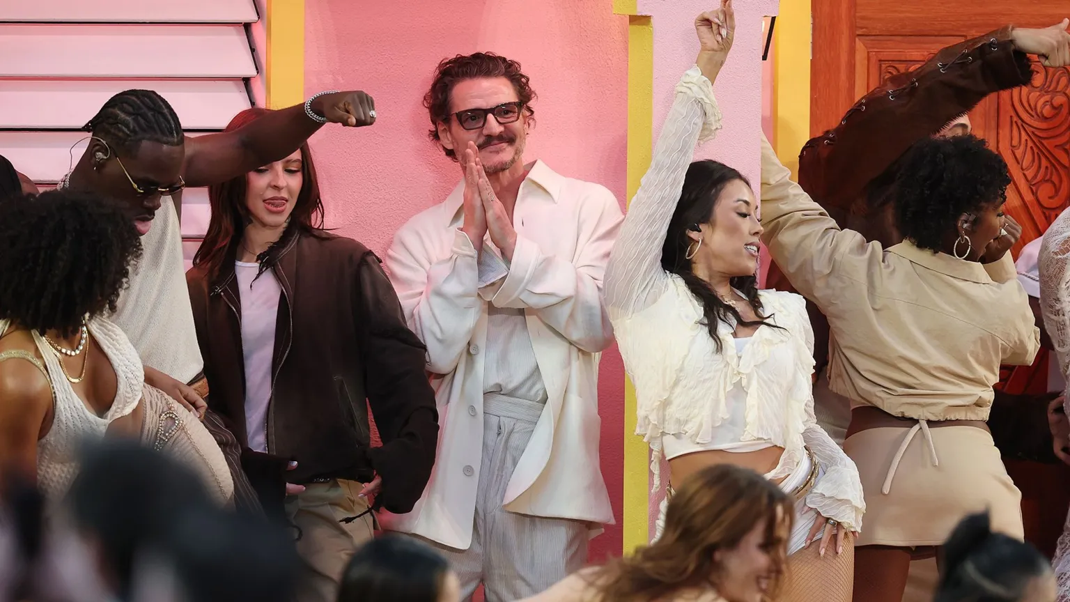  Pedro Pascal dances as Bad Bunny performs. Pedro is seen in a white suit and is smiling 