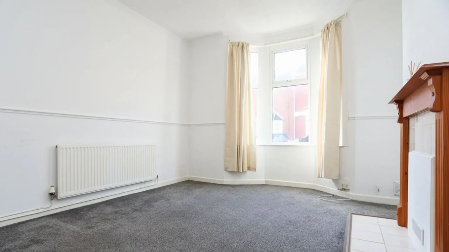 Chris Davies Estate Agents Living room with radiator on the left, window in the centre, and boarded up fireplace on the right