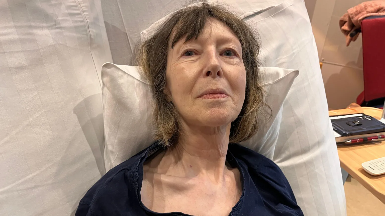 Steph Bruntlett lying in bed in the hospice. She has shoulder-length brown hair and is wearing a dark blue top.