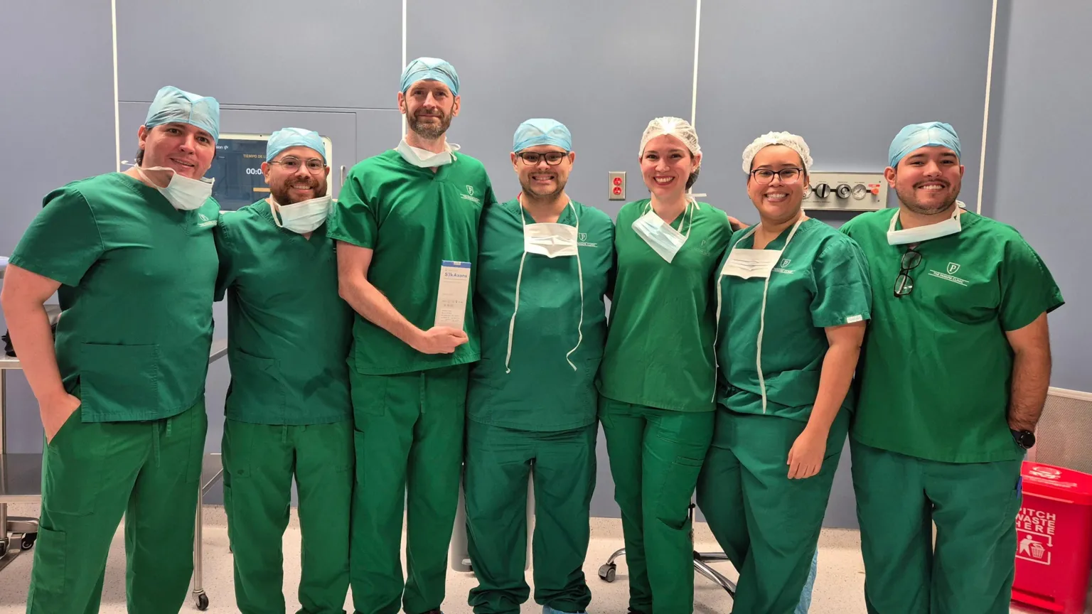 Newrotex Seven surgeons stood looking at the camera for a photo wearing green scrubs and protective equipment.