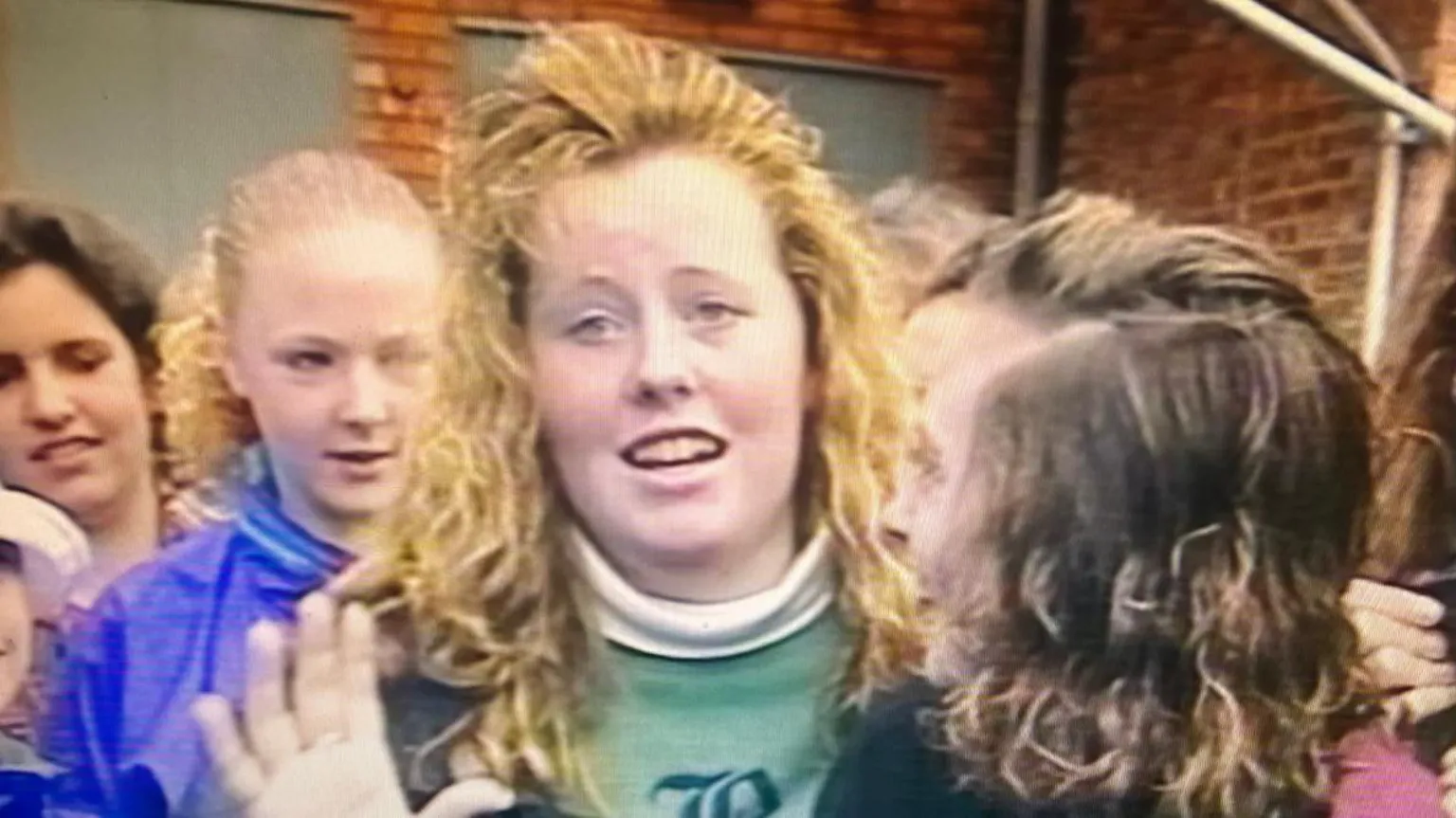Netflix A still from footage filmed in the 90s of Jemma Williamson as a teenager. She has blonde hair and a green jumper. She is in the process of talking and is in a crowd of young woman