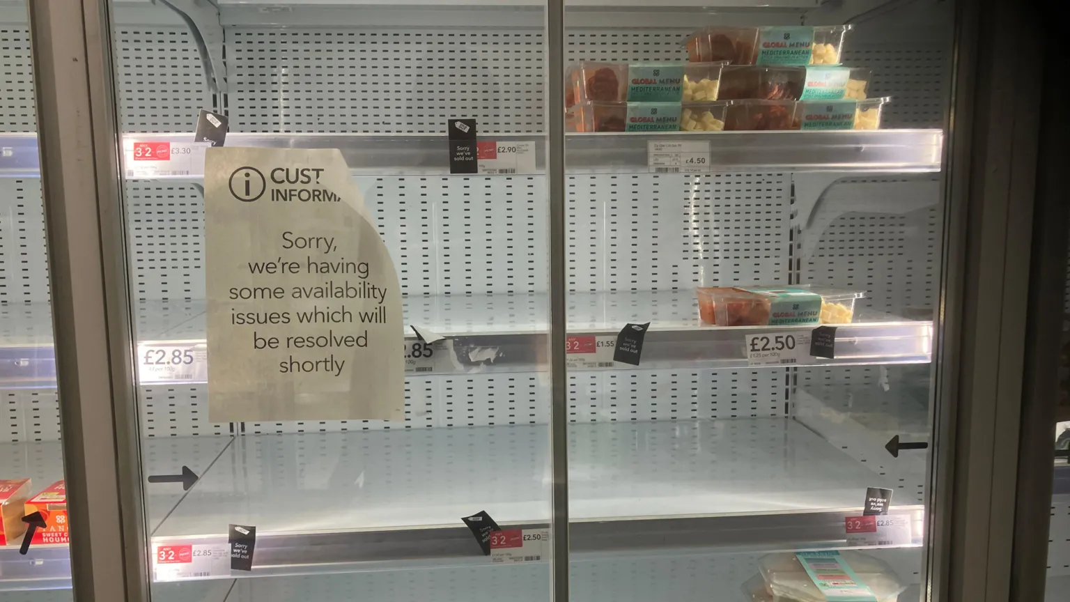 A shop fridge with almost empty shelves, and a sign stuck on the window which says