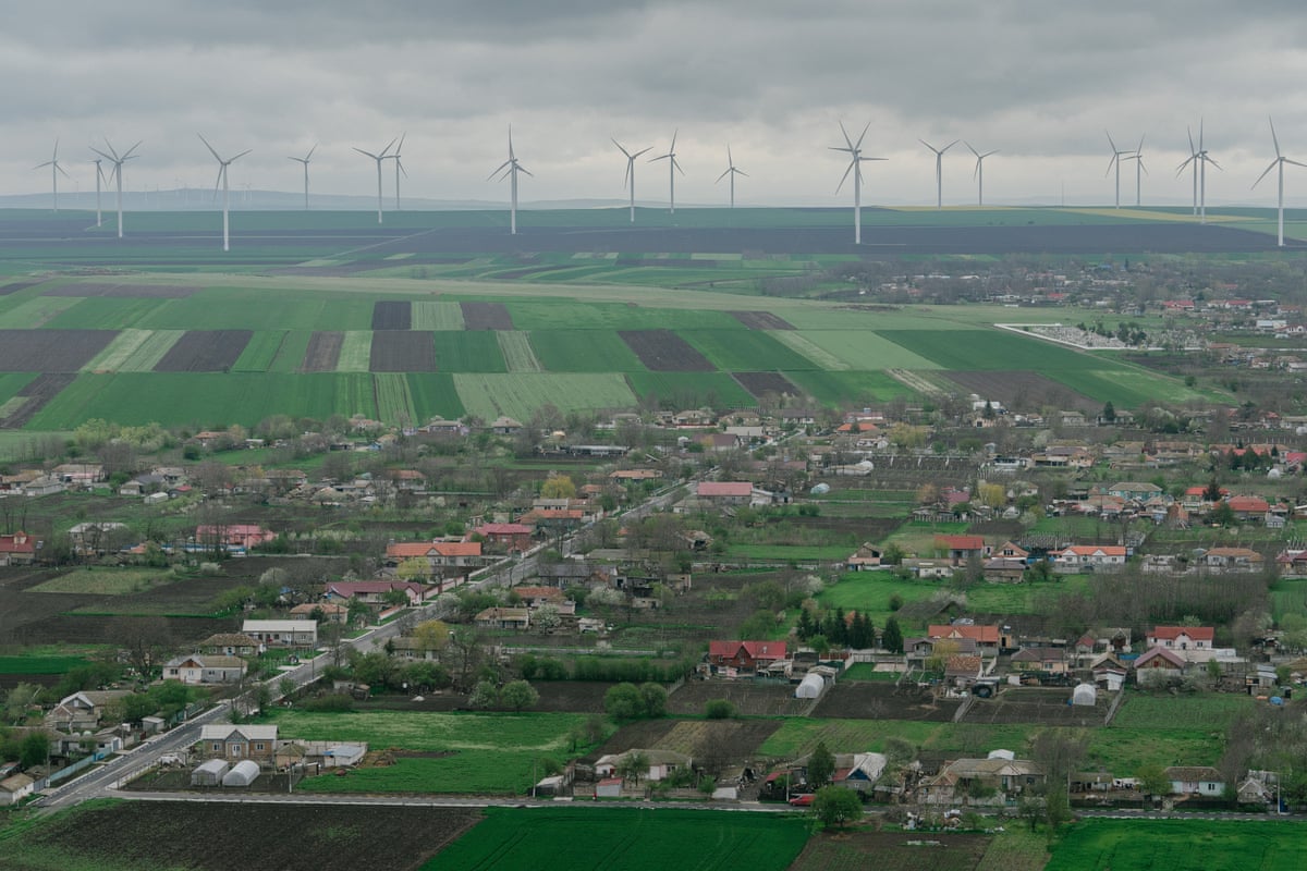 Wind turbines on grey horizon with green fields and village in foreground