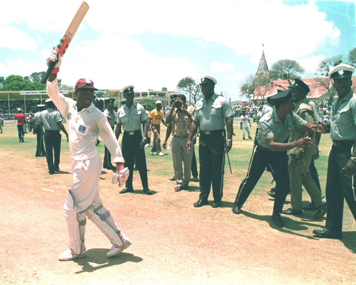 A black cricketer waves his bat to the crowd at a match as police line up to protect him