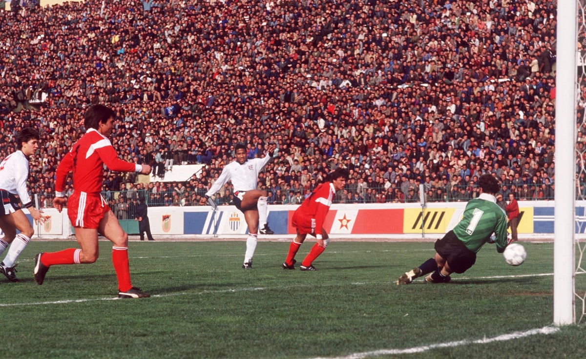 A black football player shoots past a goalkeeper as two defenders (and a young Gary Lineker) look on