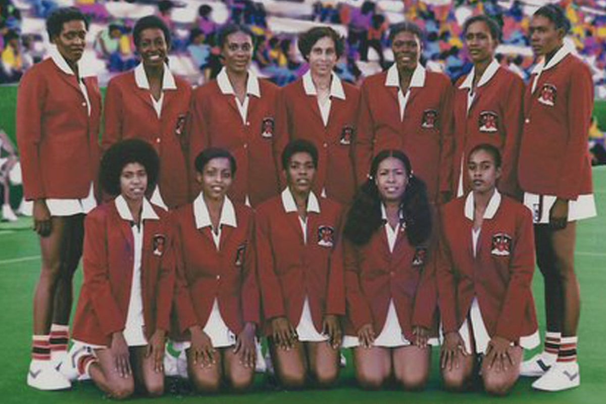 Twelve women in red jackets and white sports skirts pose in two rows.