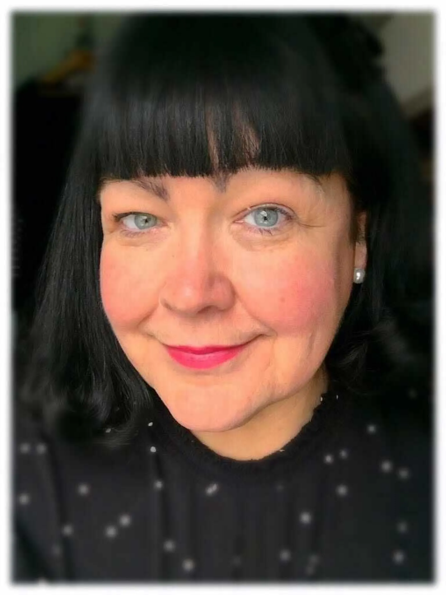 Campaign Against Living Miserably A woman with black hair and pearl earrings is looking into the camera. She is wearing a black blouse with white dots.