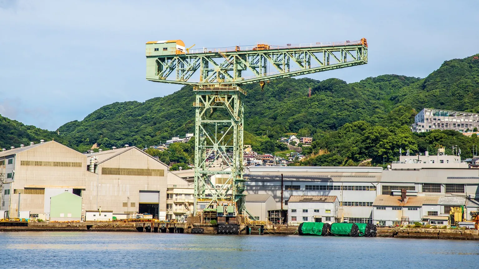  A steel latticed crane, painted in light green with industrial buildings and hills in the background