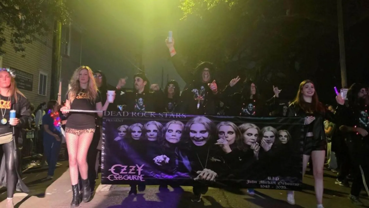 Stephen Rea A group of people holding a large banner which has faces of the singer Ozzy Osbourne. A man in the middle behind the banner is smiling with his arms raised. 