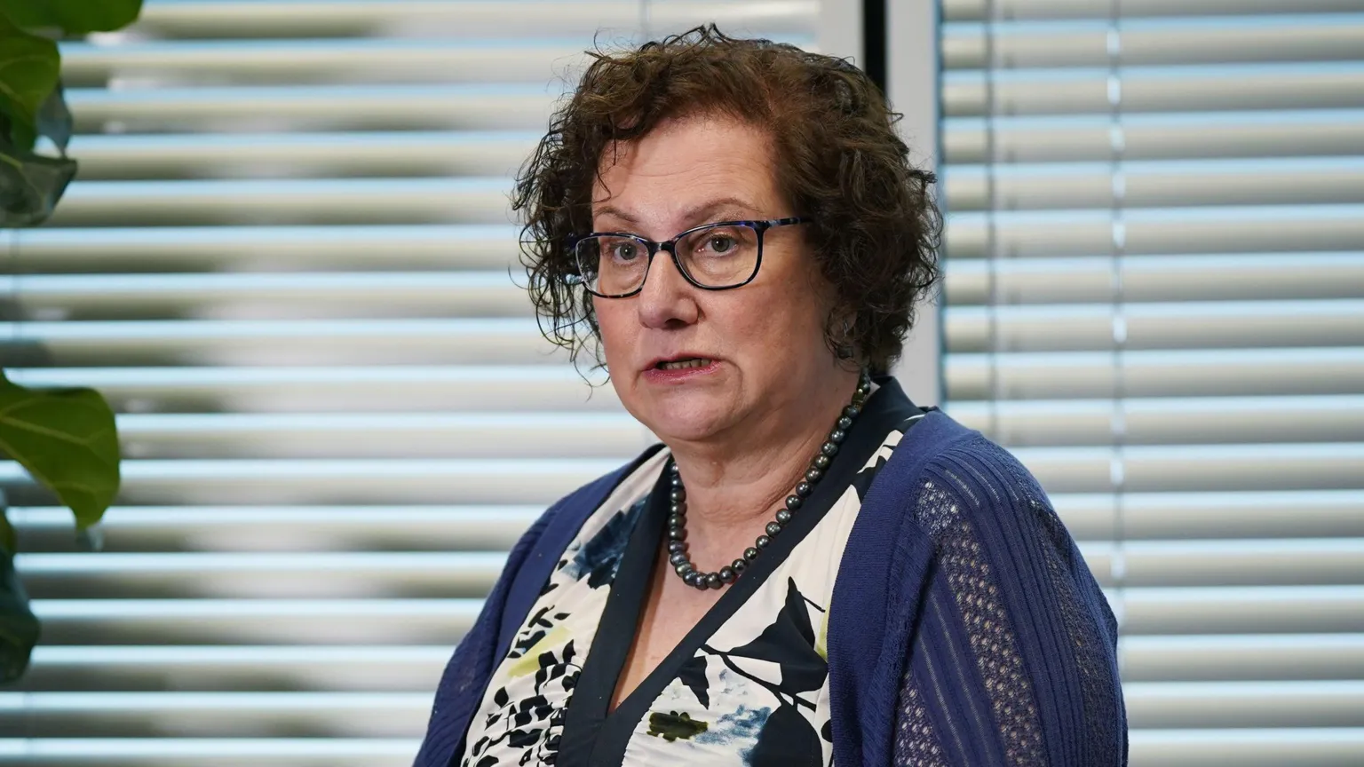  Dr Hilary Cass, wearing a white and navy dress, blue cardigan and glasses. She has short brown hair. 