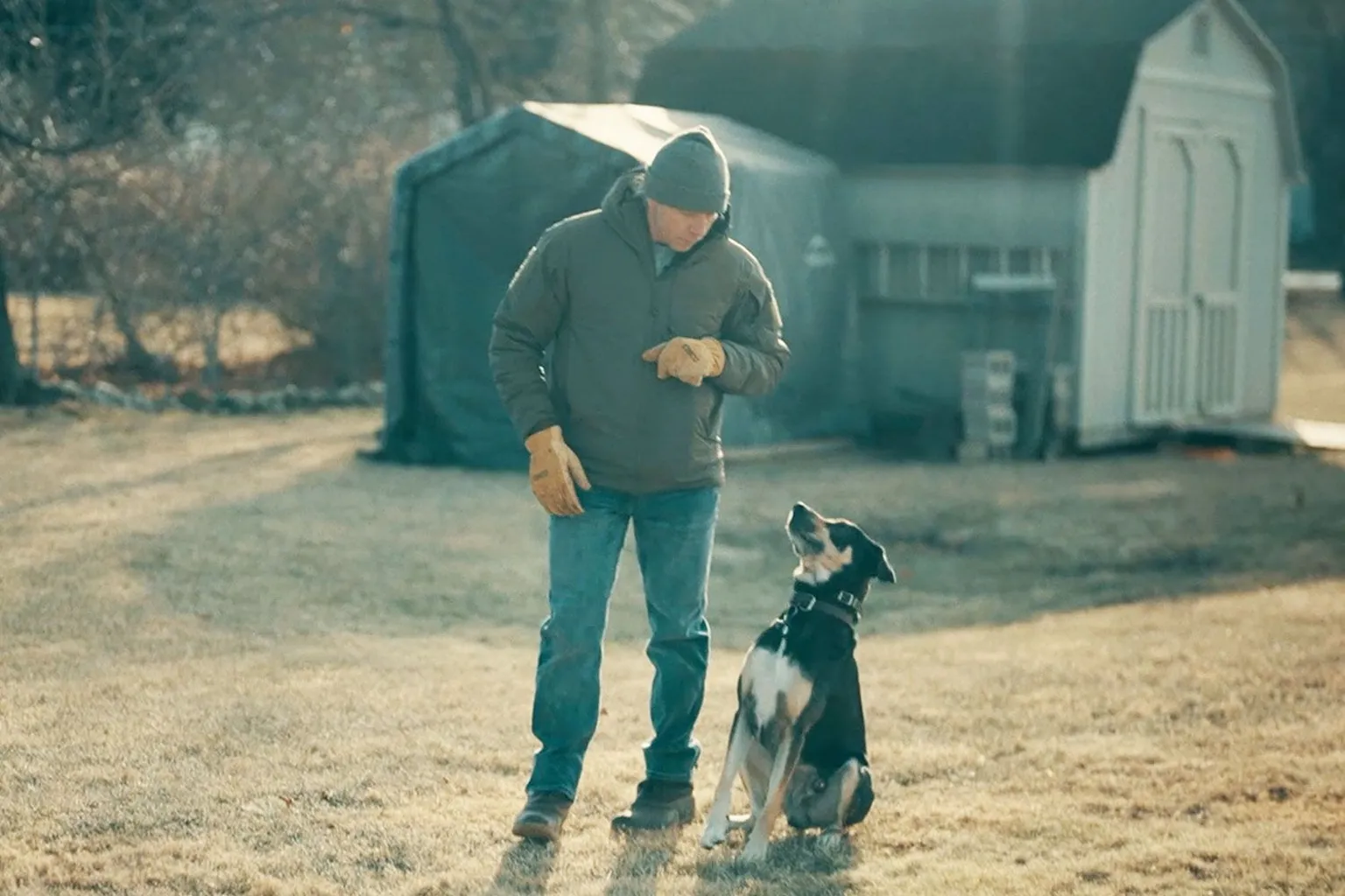 Greg Squire with his dog on a walk near his home - he is looking down at the black, white and tan dog looking up at him. 