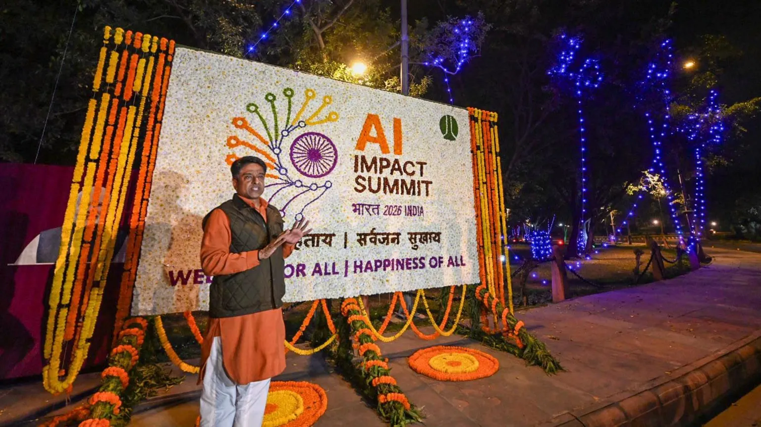  A man stands in front of an orange and white sign which reads 