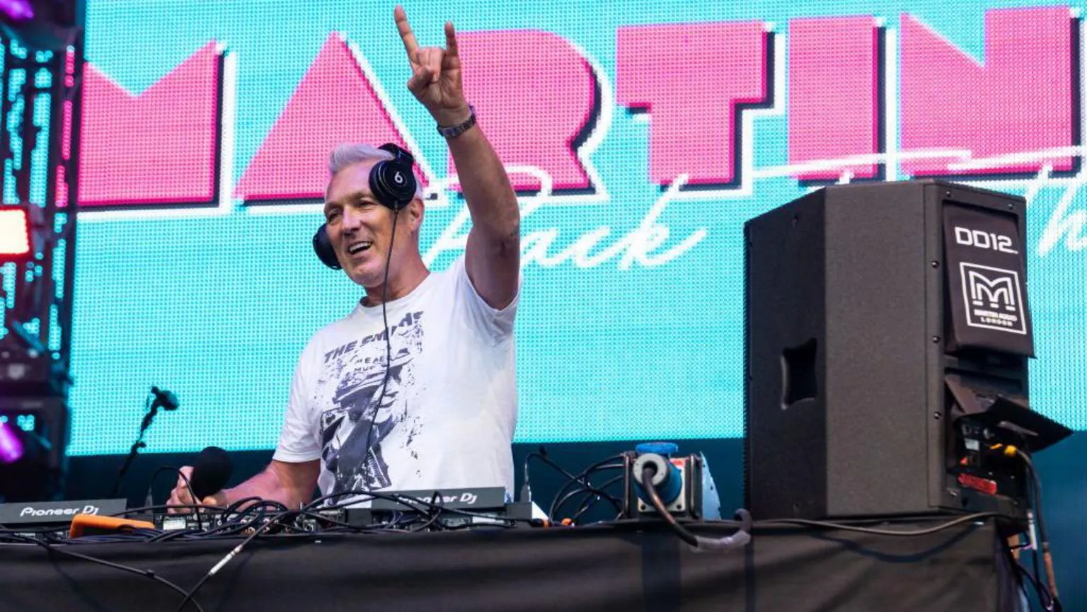  Musician Martin Kemp standing behind some DJ decks, wearing headphones and holding a 