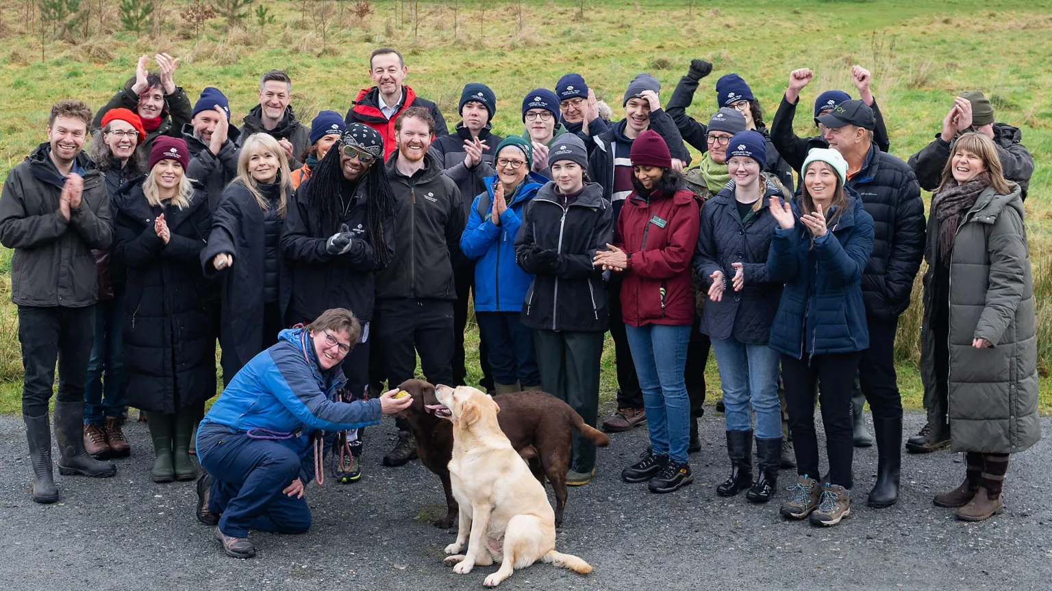 The Woodland Trust A crowd of people in outdoor wear surround Nile Rogers and two Labrador dogs sit in front of them