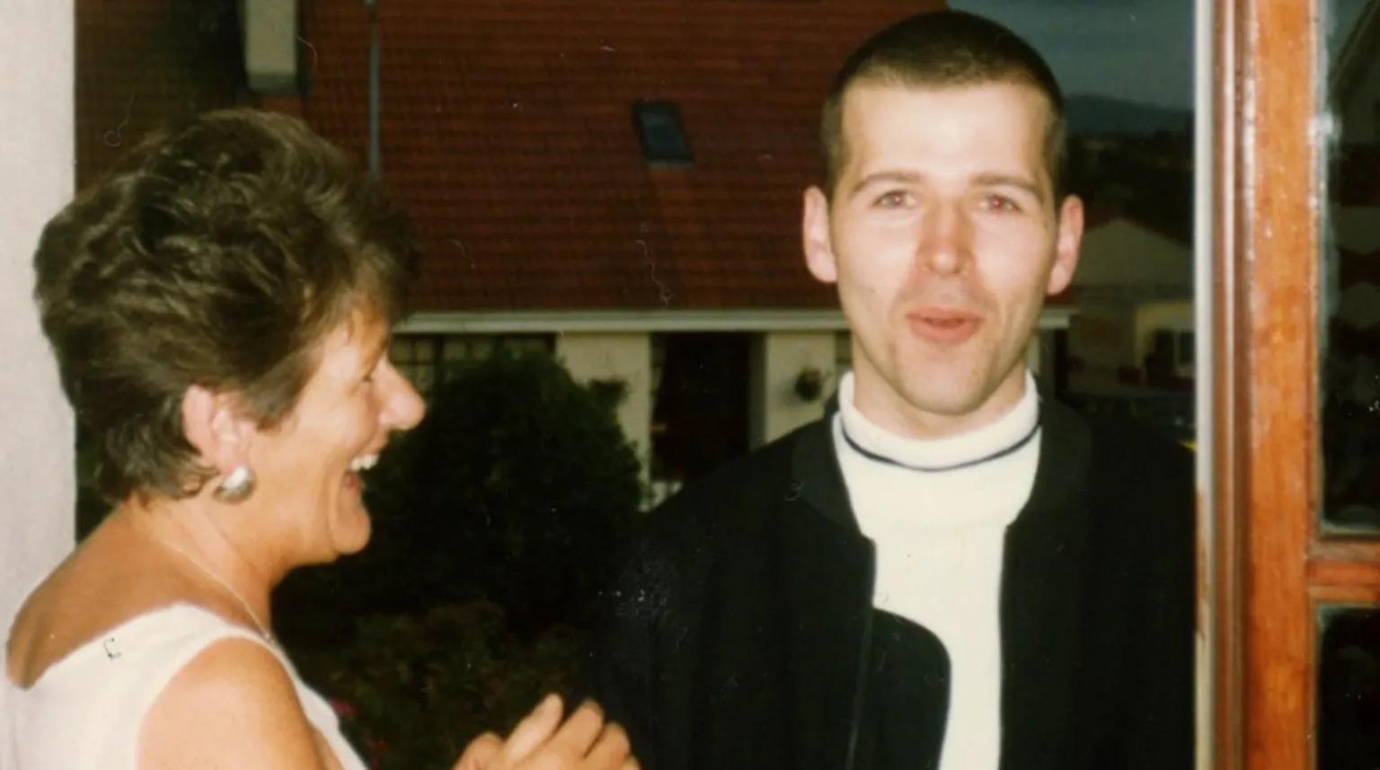 Peter Cunnah Shows a profile view of woman on the left with short dark hair and a light top. She is laughing. To the right is a young man with short hair in a white top and black jacket. He is looking at the camera. 