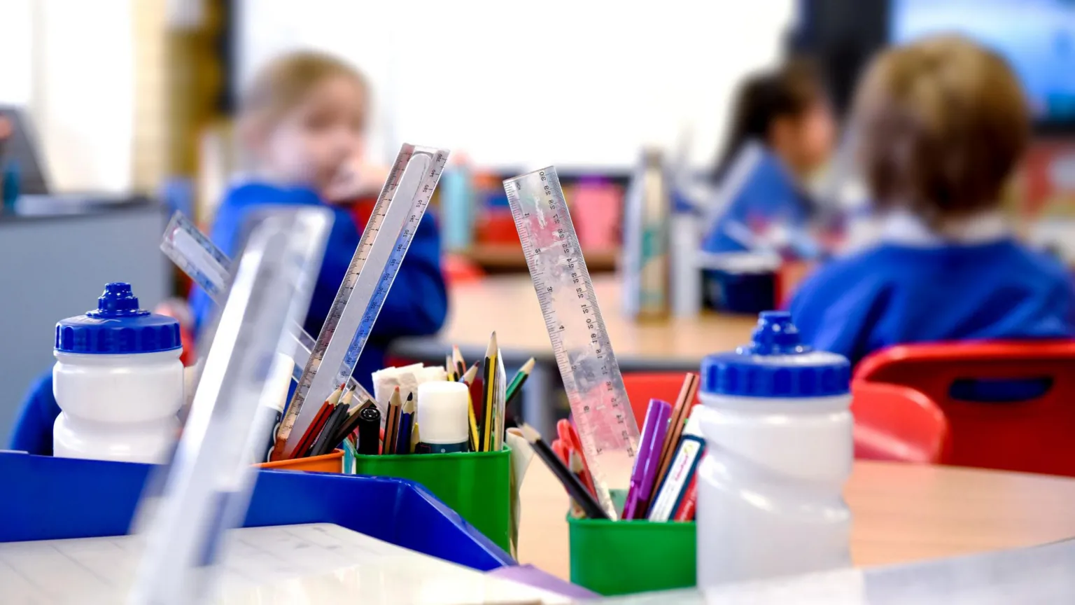 A stock image of a school with pencils, rulers, cups and bottles on the desk