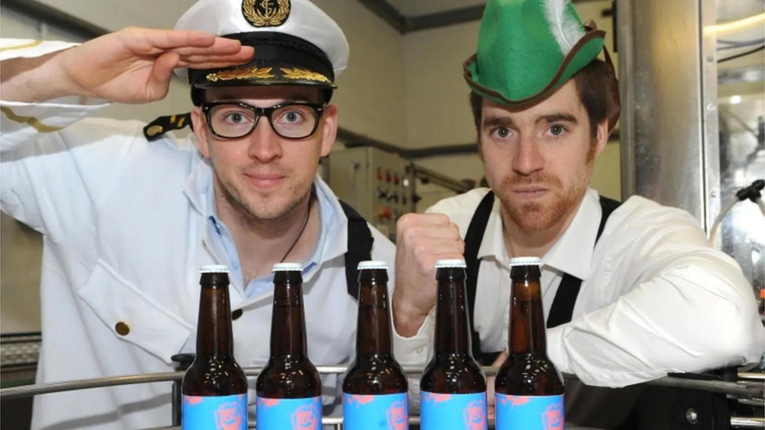 Brewdog A man dressed as a sea captain next to a man wearing a green hat, posing for a photograph in front of bottles of beer