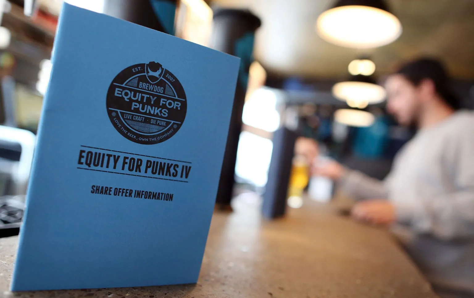  A blue Equity for Punks IV share offer booklet sitting on a table in a bar