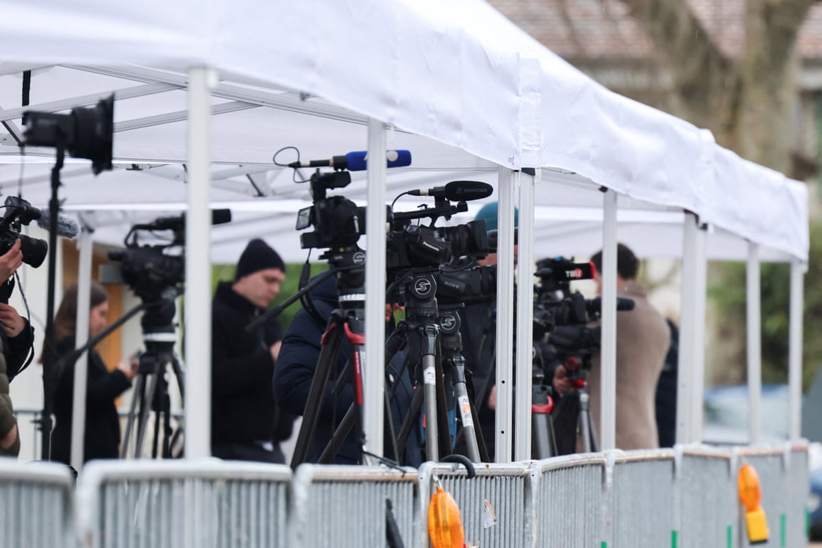Multiple cameras on tripods under a tented area sectioned off for the press.