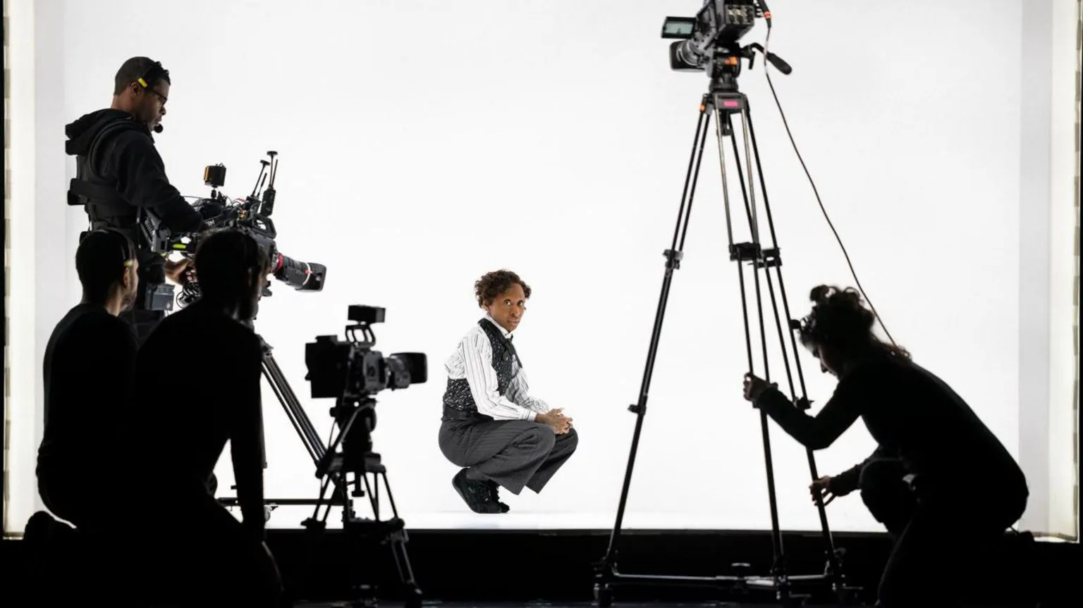 Daniel Boud Cynthia Erivo dressed in a suit on stage against a white backdrop with three cameras pointing at her. 