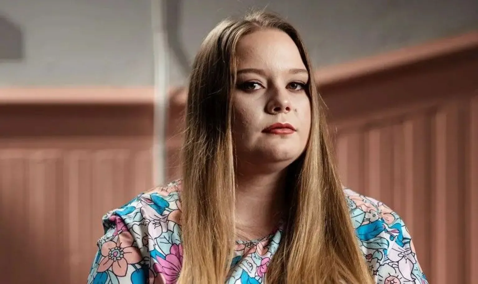 Gavin Hopkins White young woman with dark blonde hair with a floral dress on against a pink and white background.