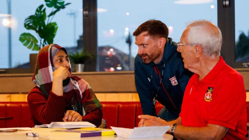 Tri person yn eistedd wrth fwrdd