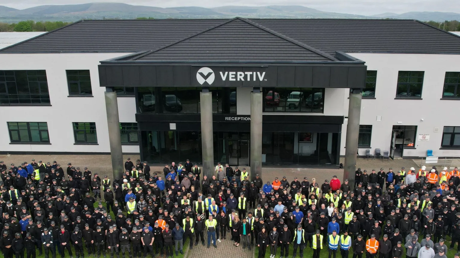 Vertiv A crowd of people are standing outside a large black and white building with a Vertiv sign at the top.