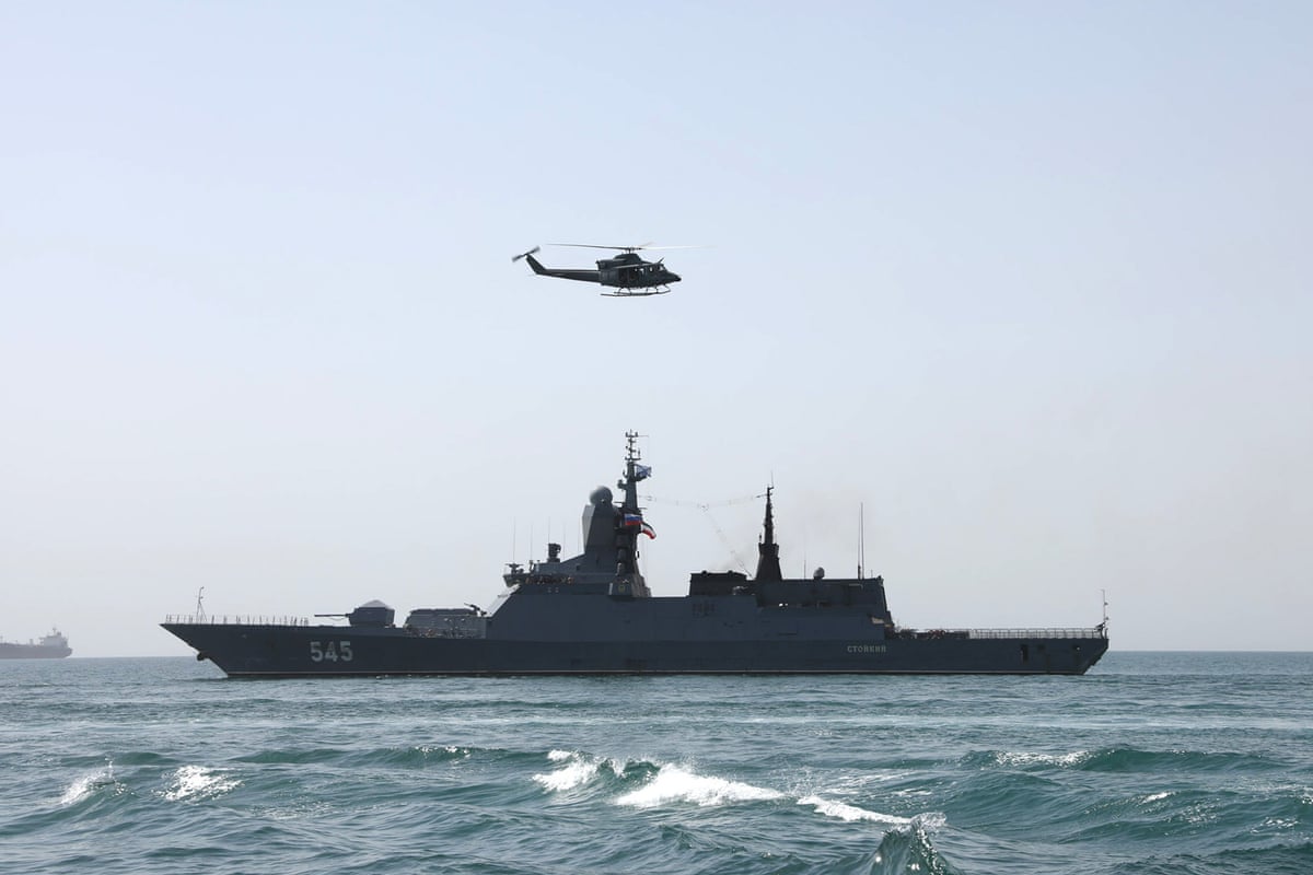 A warship at sea with a helicopter overhead. 