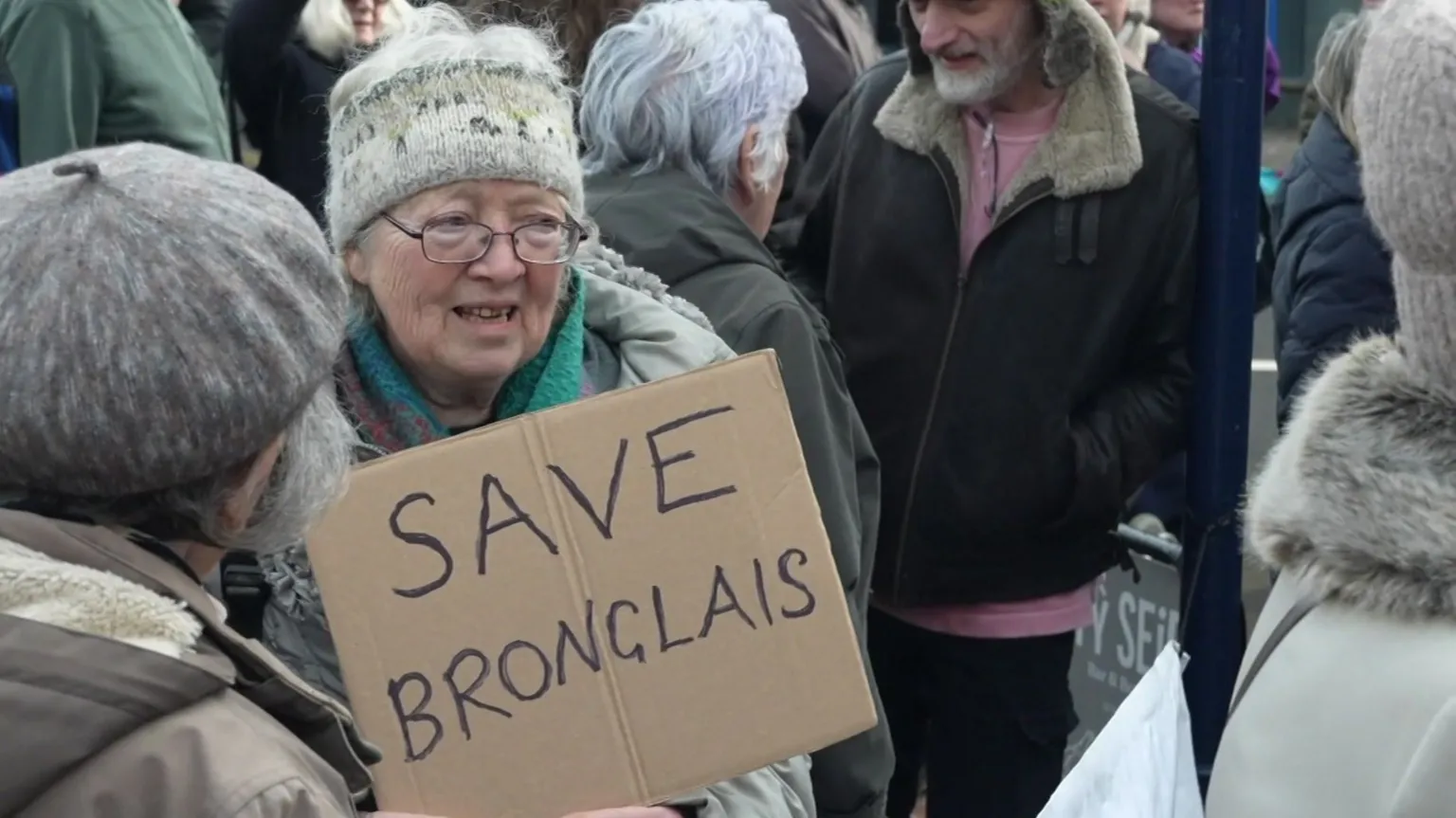 A woman standing amongst a crowd of protestors. She is holding up a cardboard sign with 