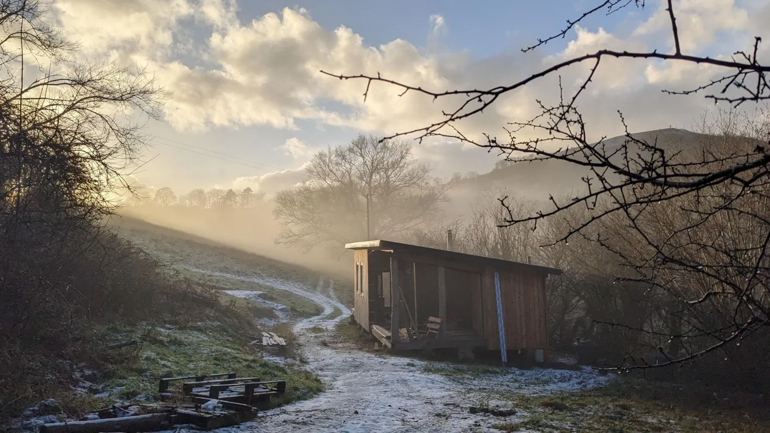 Under Starry Skies The image shows a wooden log cabin, in a frosty nature scene with the sun rising and hills and a field behind it. 