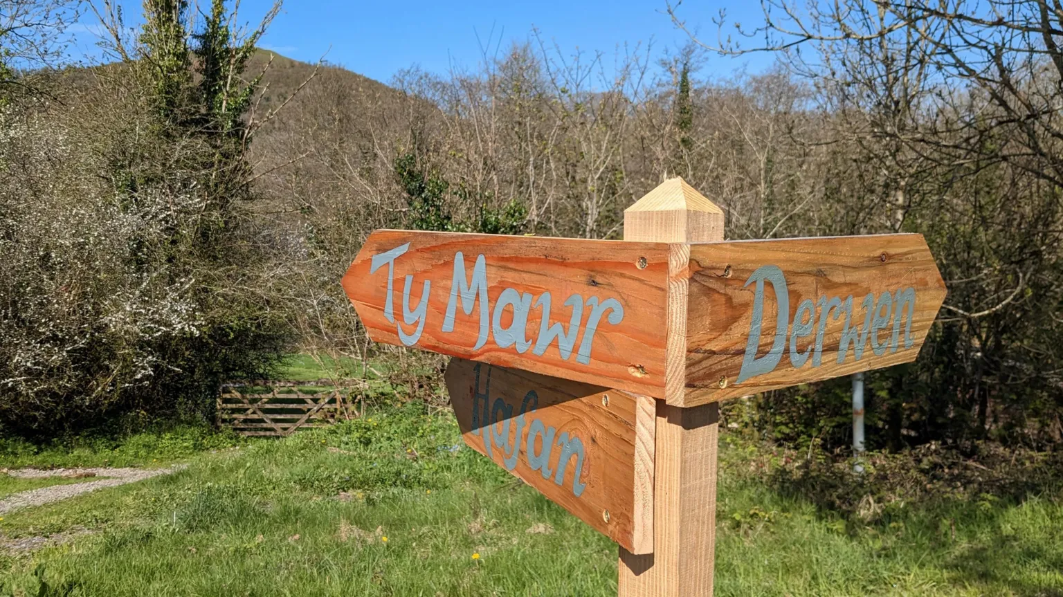Under Starry Skies A wooden signpost directing visitors to different parts of the nature reserve. The background shows clear blue skies and greenery of the nature reserve. 