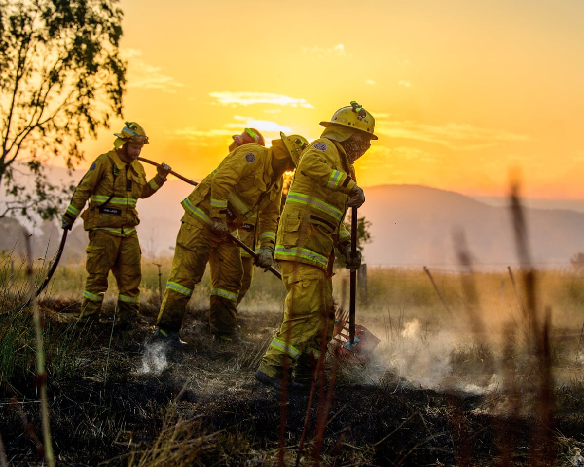 Firefighter wearing protective gear standing on burnt-out grass with a bright yellow sky behind