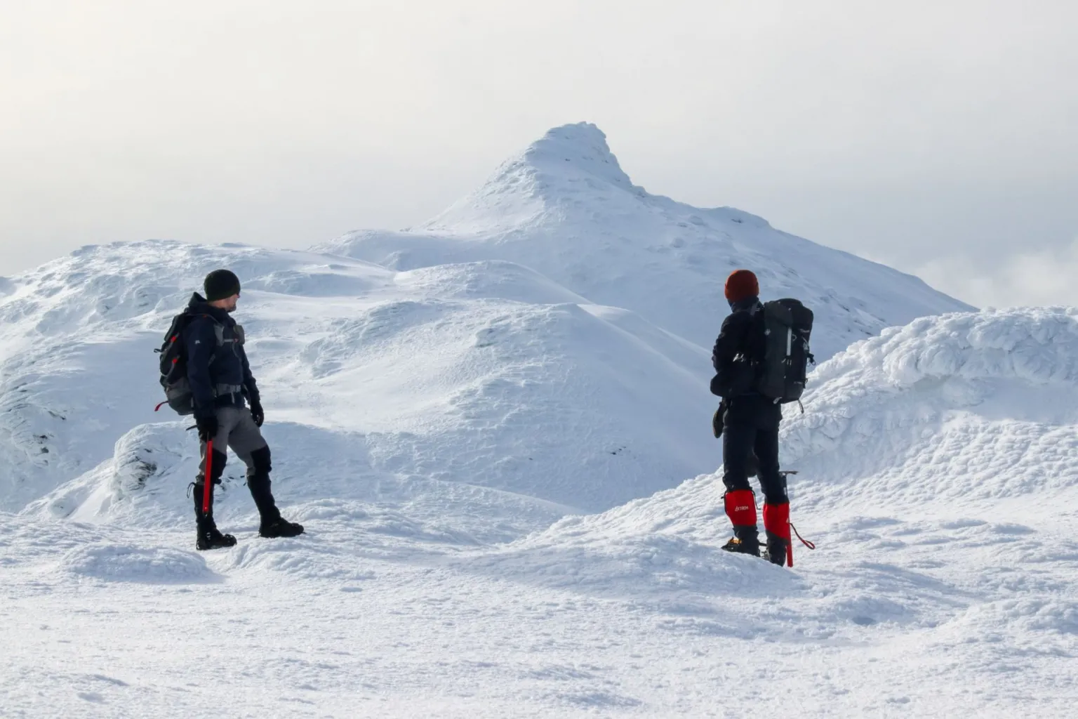 Gareth Overton Two mountaineers with rucksacks and winter gear are looking towards a snowy peak
